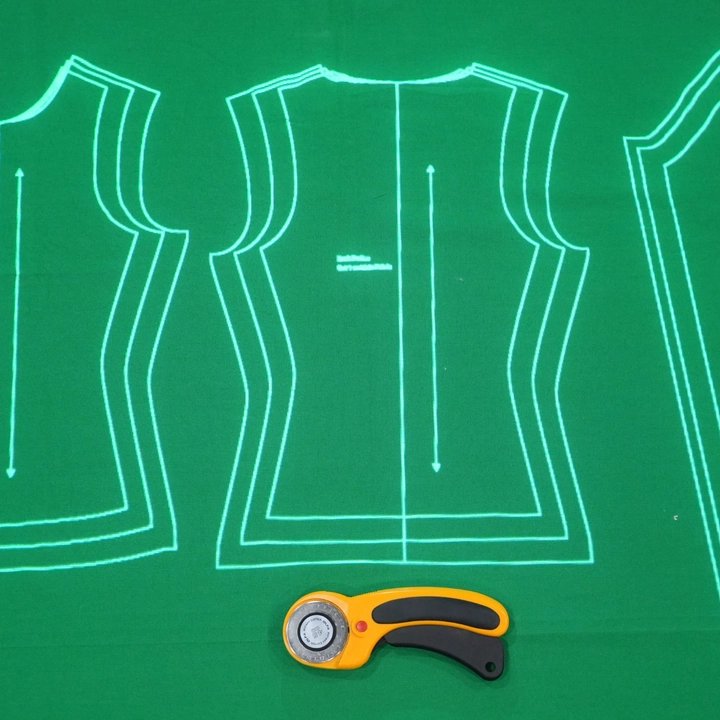 A sewing pattern projected onto green fabric, with a rotary cutter ready for cutting